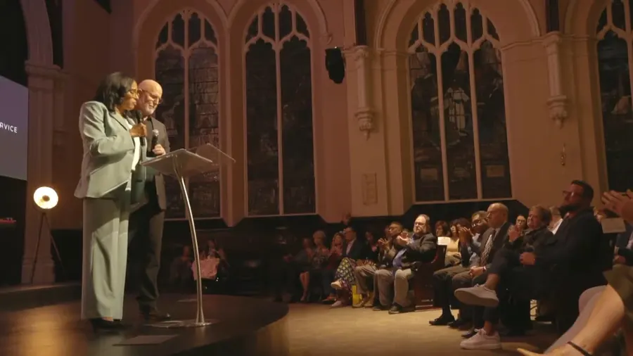 Two speakers at the podium seen from the side of the stage, with the congregation beyond them