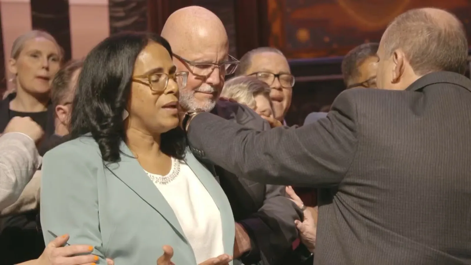 People on stage with their hands on the shoulders of a couple, praying over them
