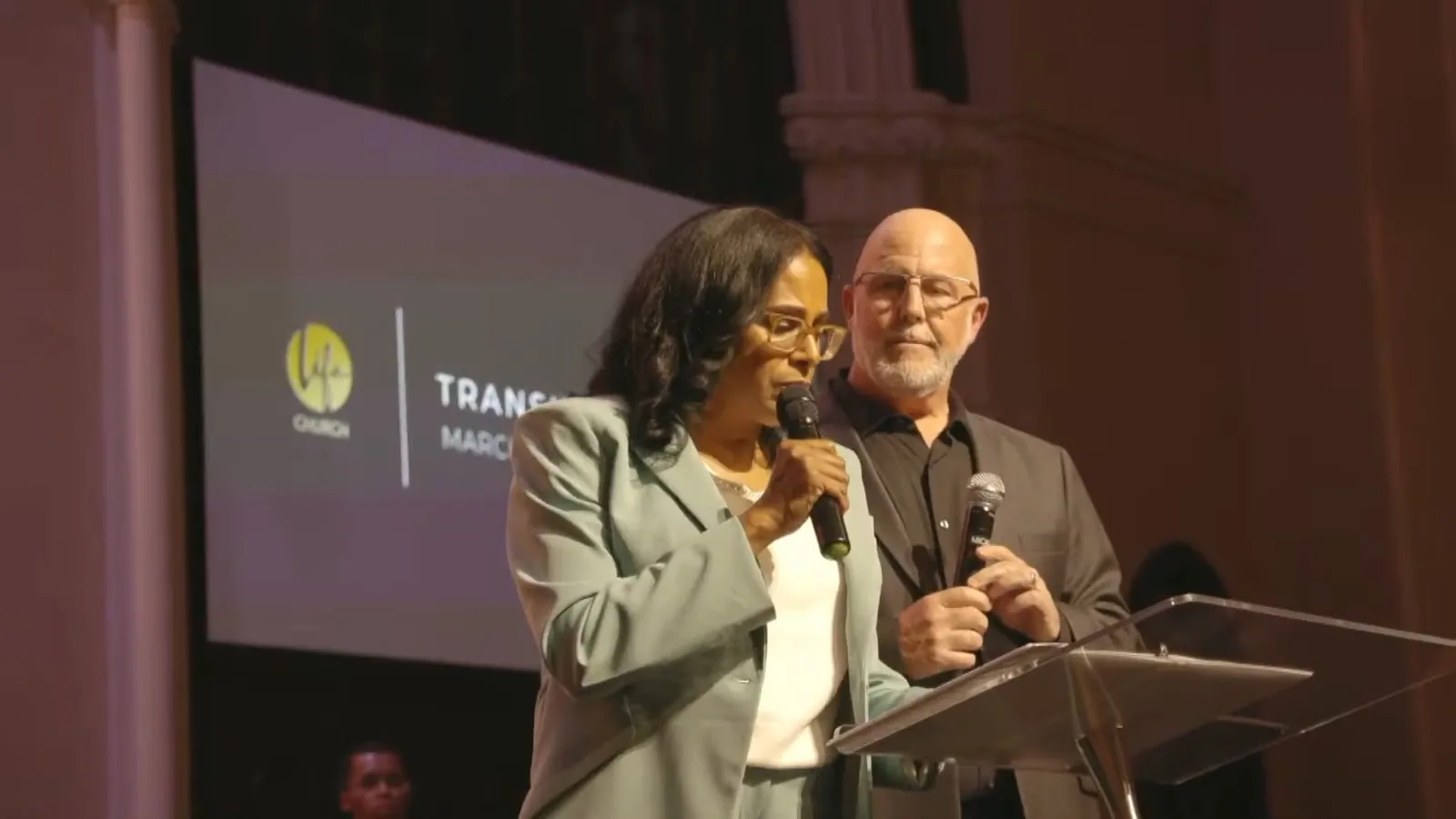 Two pastors at the podium with the Transition Service slide on the screen behind them