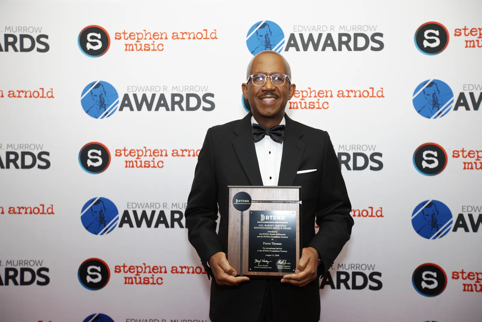 Pierre Thomas of ABC News in a tuxedo, smiling and holding his framed Barney Oldfield Distinguished Service Award plaque in front of the Murrow Awards backdrop