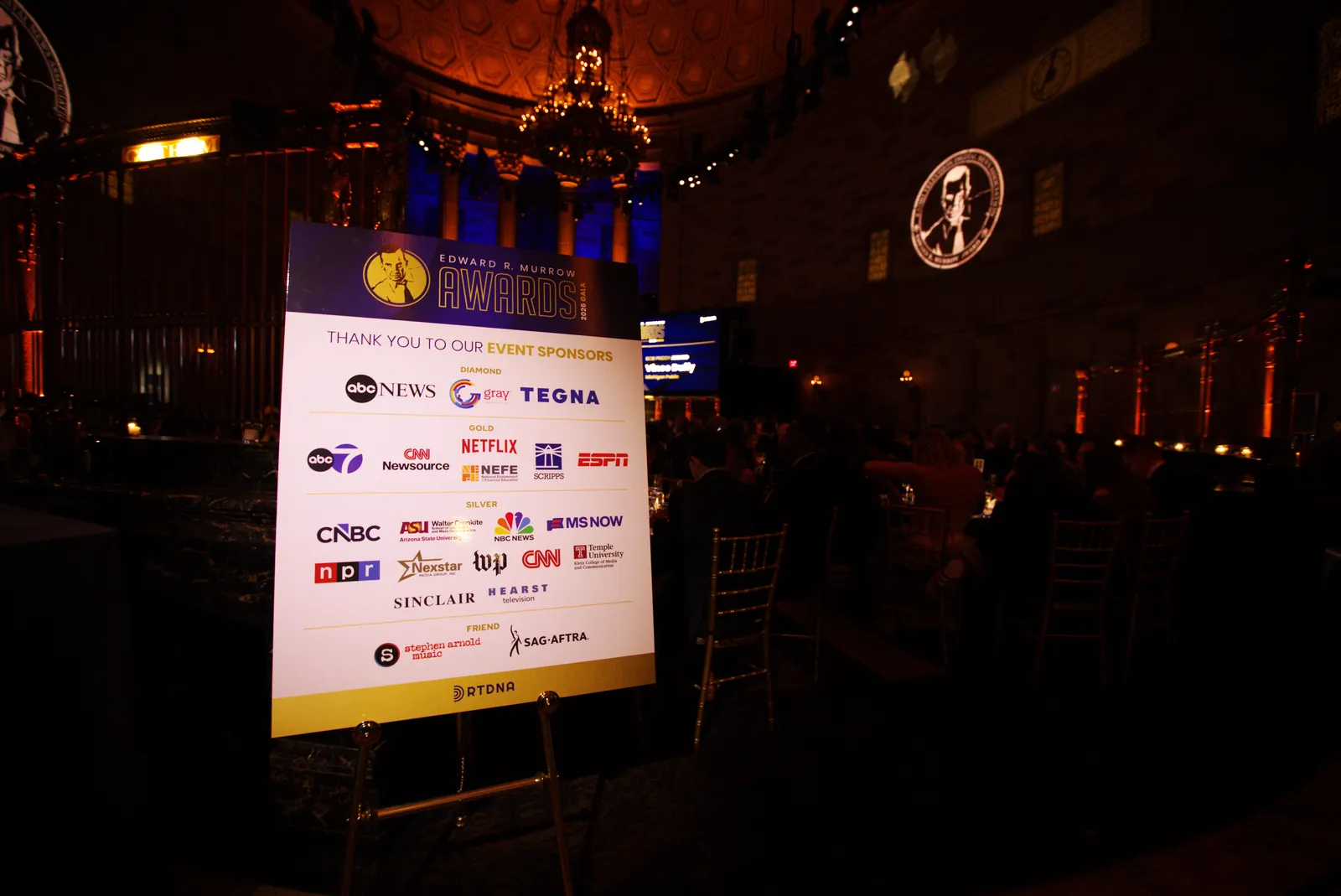 The event sponsor board on an easel in the darkened ballroom listing the gala sponsors