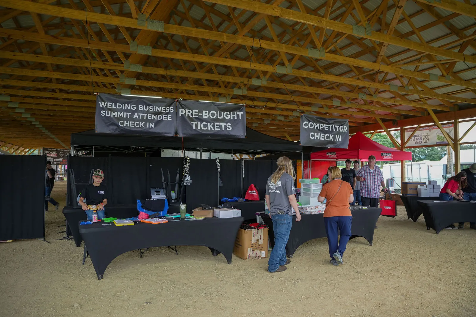 Check-in tents under the pavilion with signs for Welding Business Summit attendee check-in, pre-bought tickets and competitor check-in