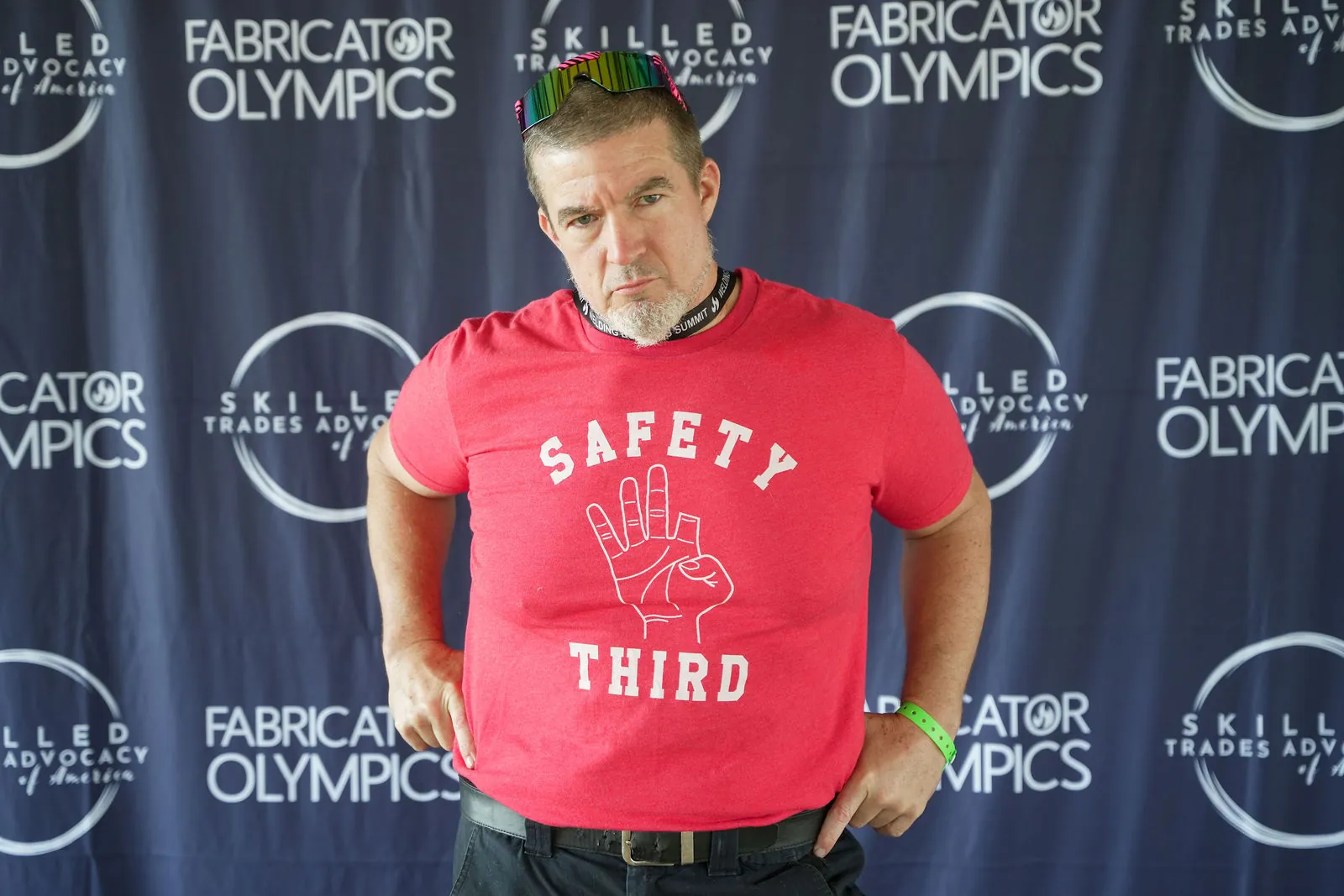 A competitor in a red Safety Third shirt with his arms at his sides in front of the Fabricator Olympics backdrop