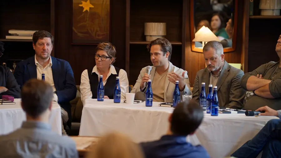 Panelists at the left table in front of the bookshelves, one of them speaking