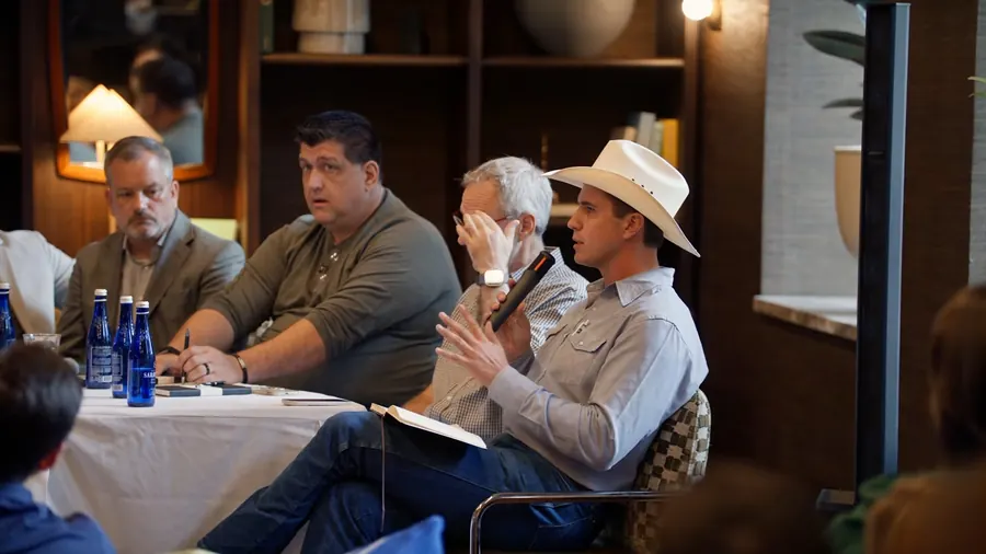 A panelist in a white cowboy hat holding a microphone at the right table