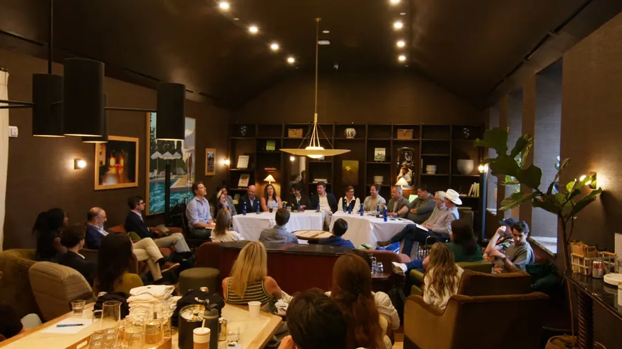 The whole room from the back, with the audience in armchairs and both tables at the far end