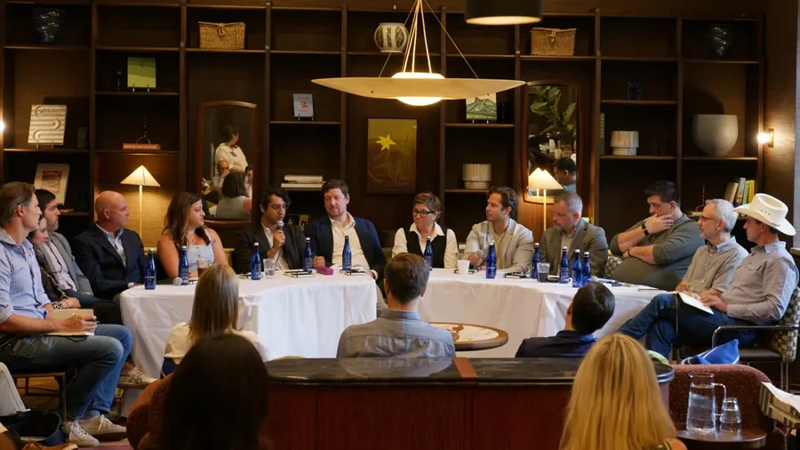 Every panelist across both round tables, seen over the heads of the front row