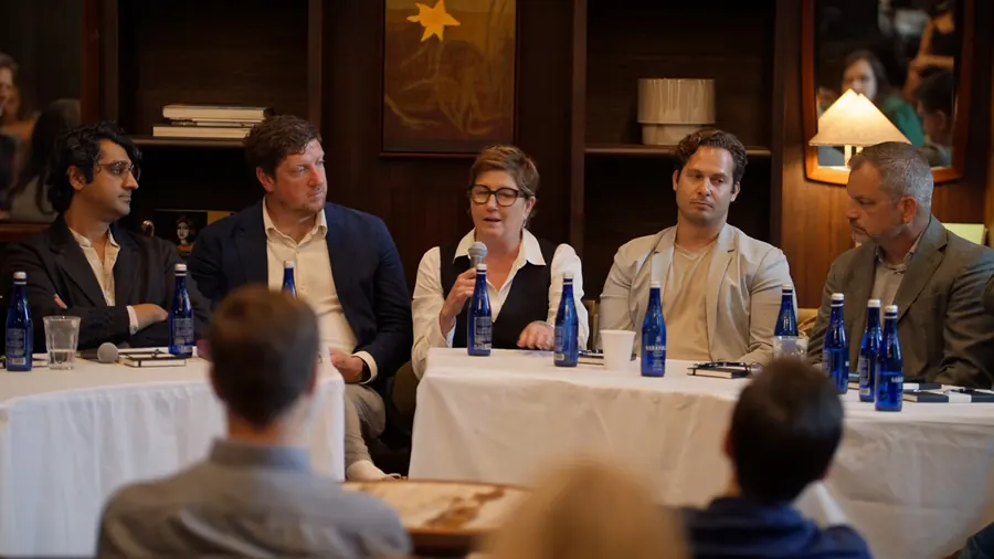 A panelist at the left table speaking into a microphone with blue water bottles on the table