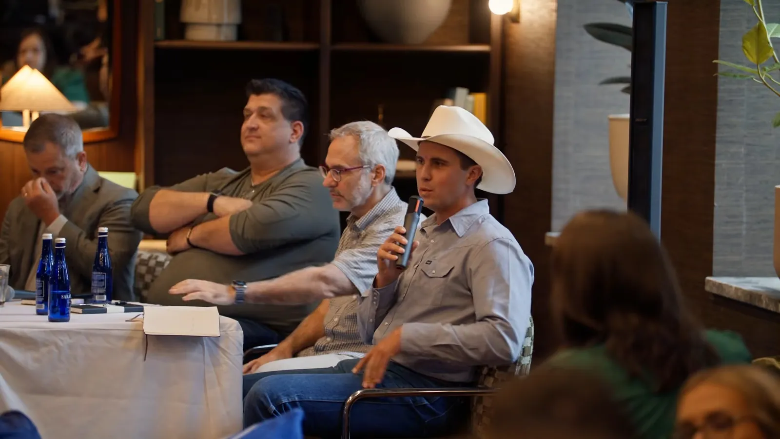 A panelist in a white cowboy hat speaking into a microphone at the right table