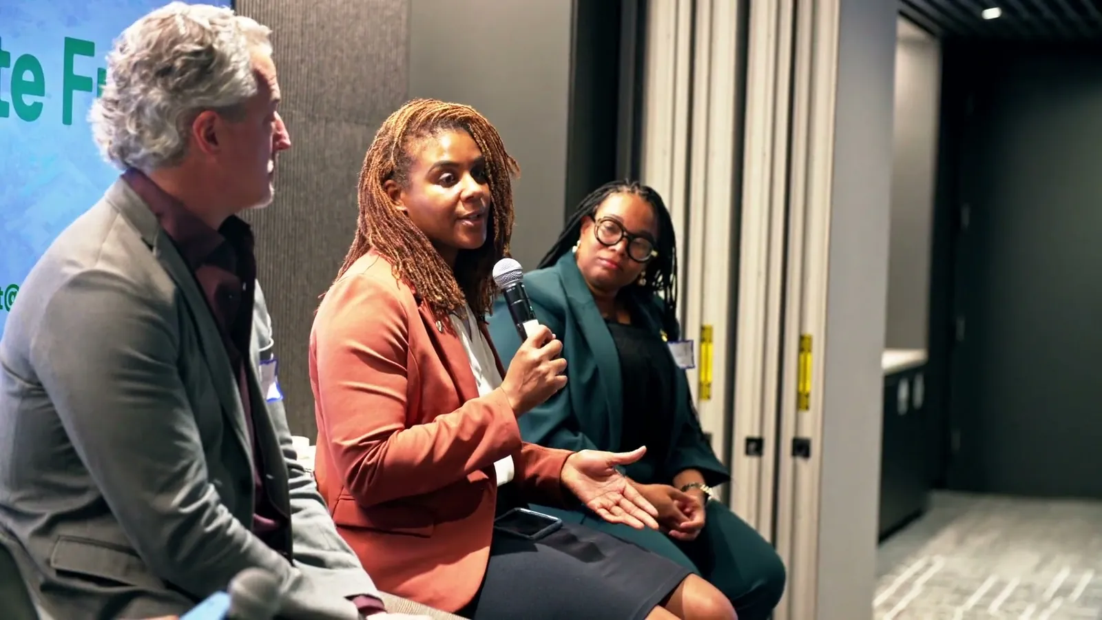 Three panelists seated close together, one of them speaking into a microphone