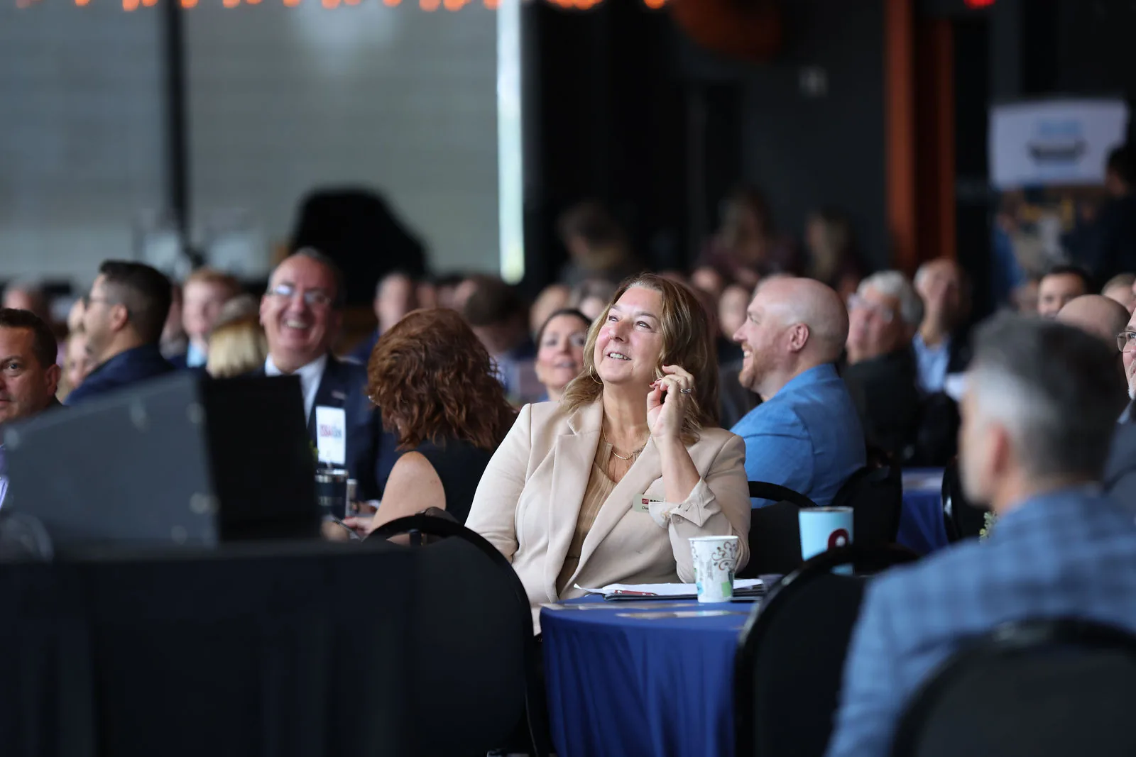 Attendees at their tables laughing during a talk, faces to the camera