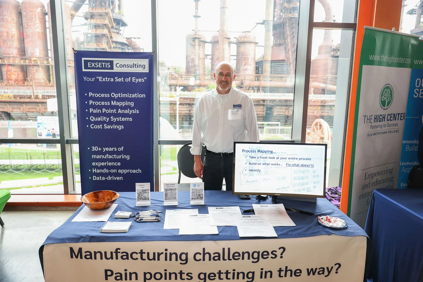 An exhibitor at his table with the Bethlehem Steel blast furnaces visible through the windows behind him