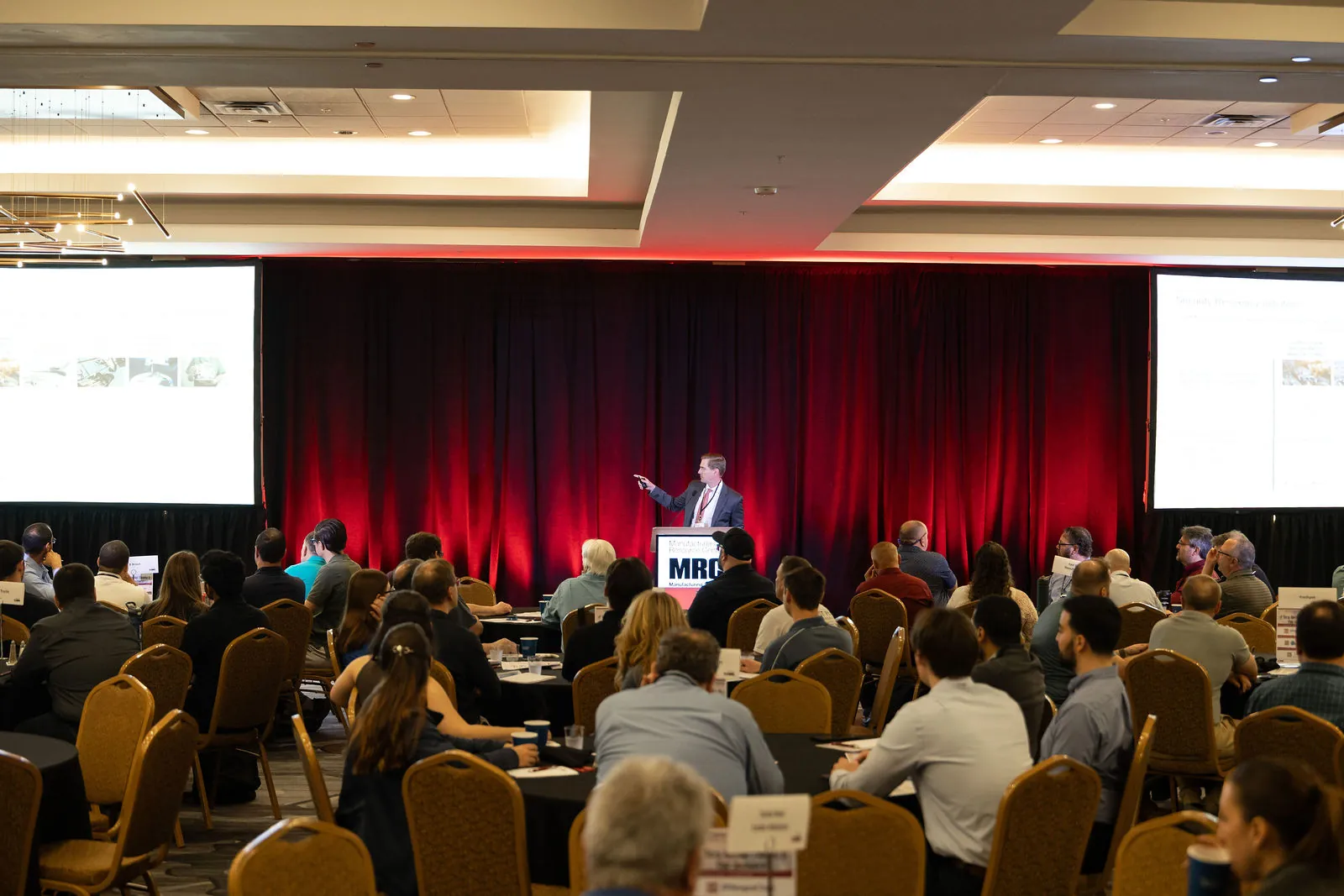 The full ballroom from the back during a presentation, with red curtains and screens on either side of the stage