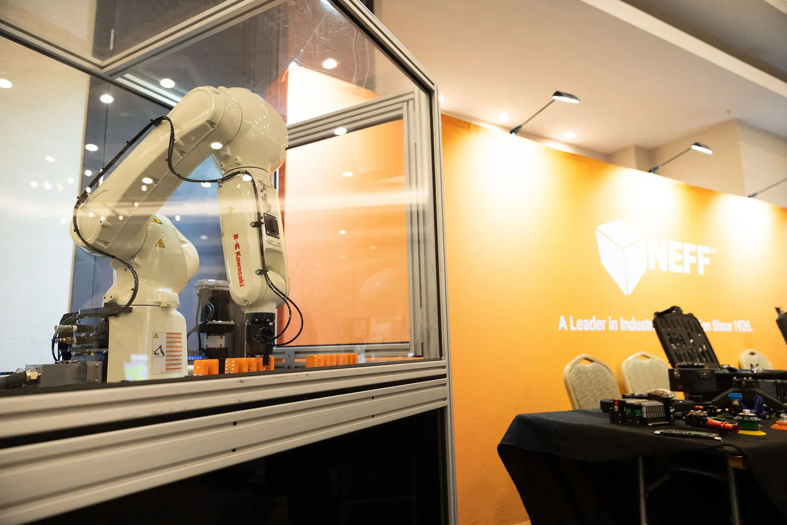 A Kawasaki robot arm inside a clear enclosure at the Neff booth