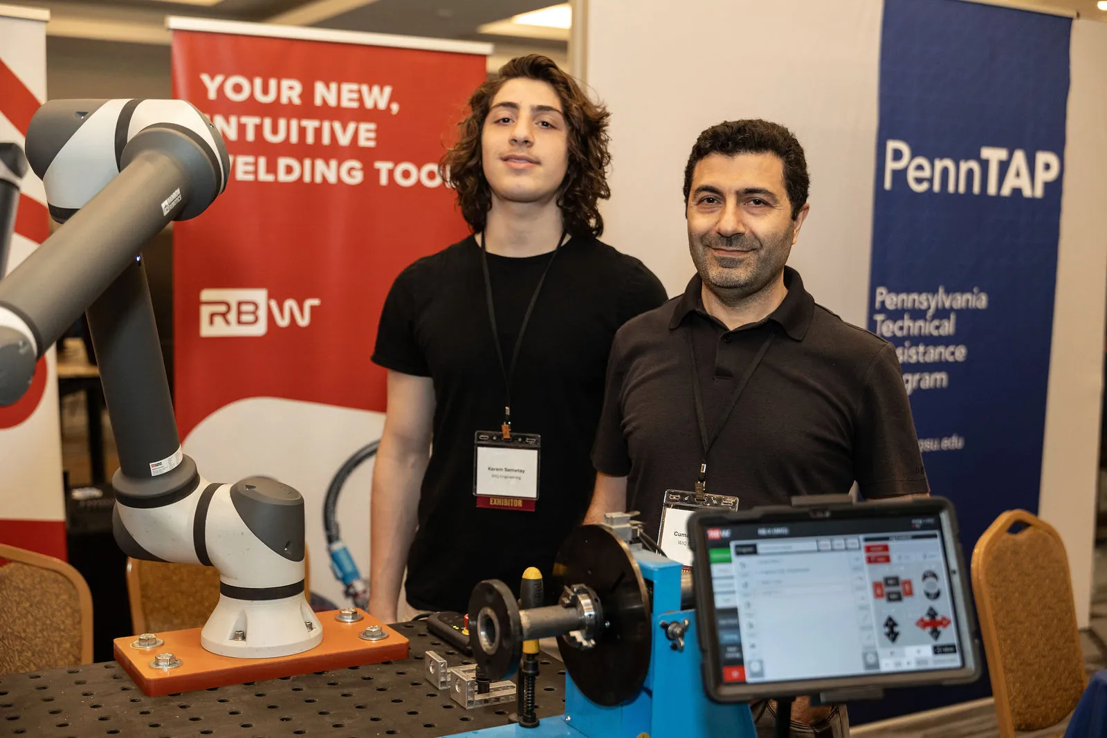 A collaborative welding robot demo with two exhibitors standing behind it