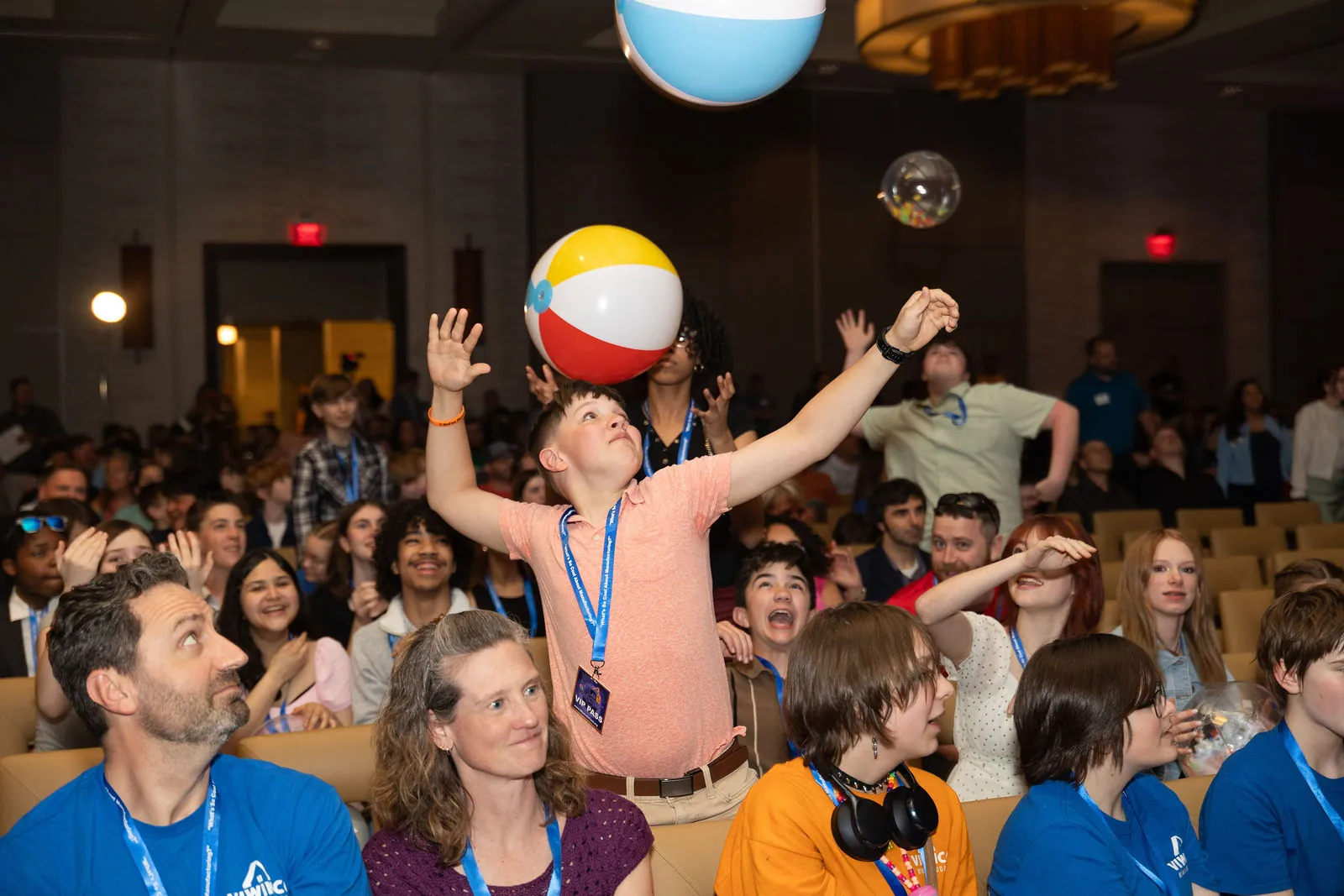 A student in the crowd with his arms up as a beach ball flies over the seats