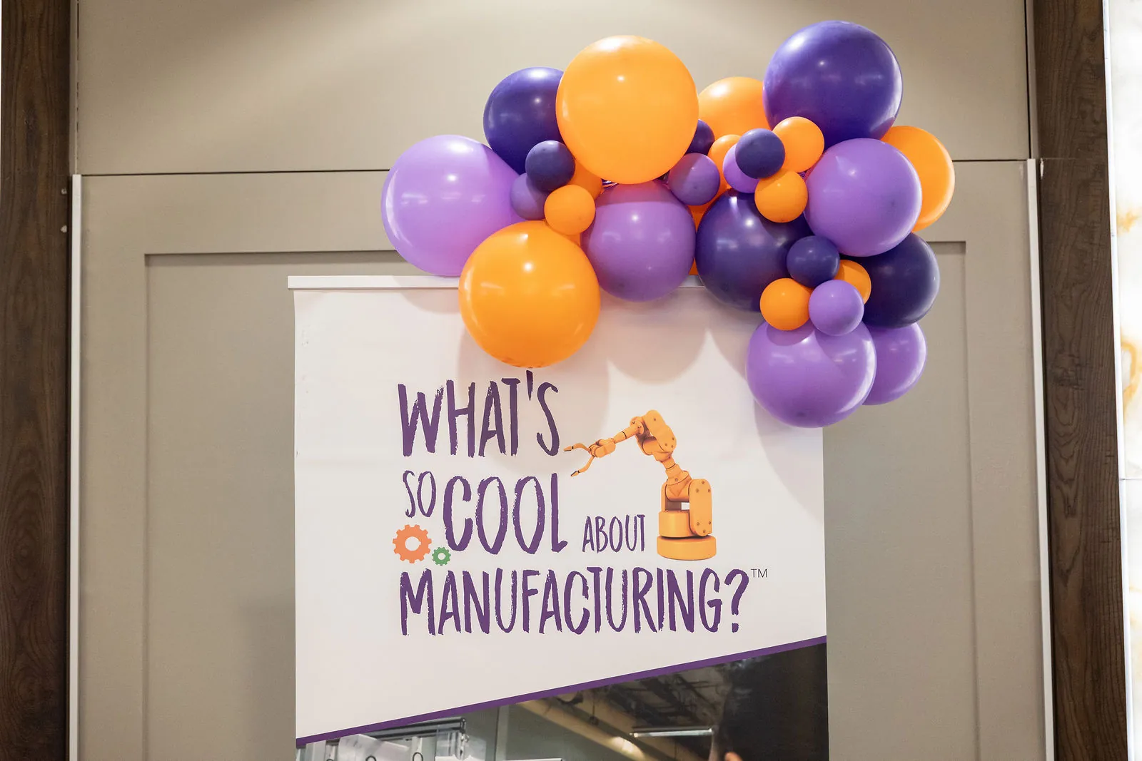 A What's So Cool About Manufacturing banner topped with purple and orange balloons