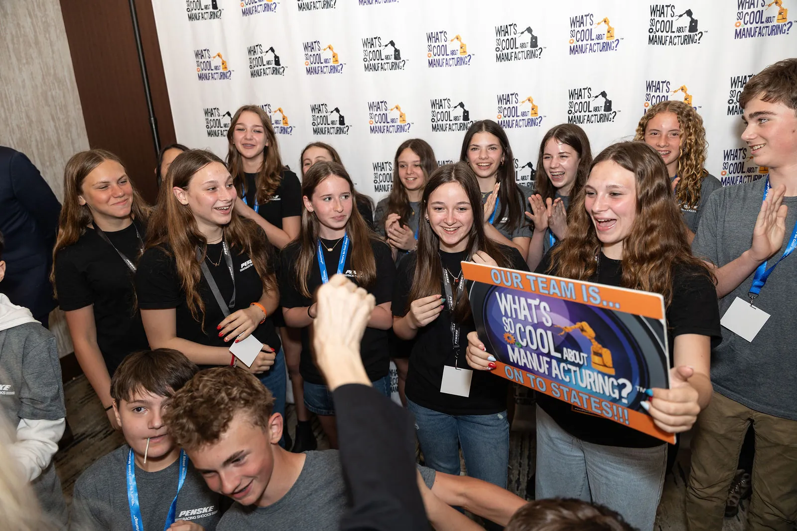 A team of students in black shirts cheering and holding up a contest sign at the step and repeat