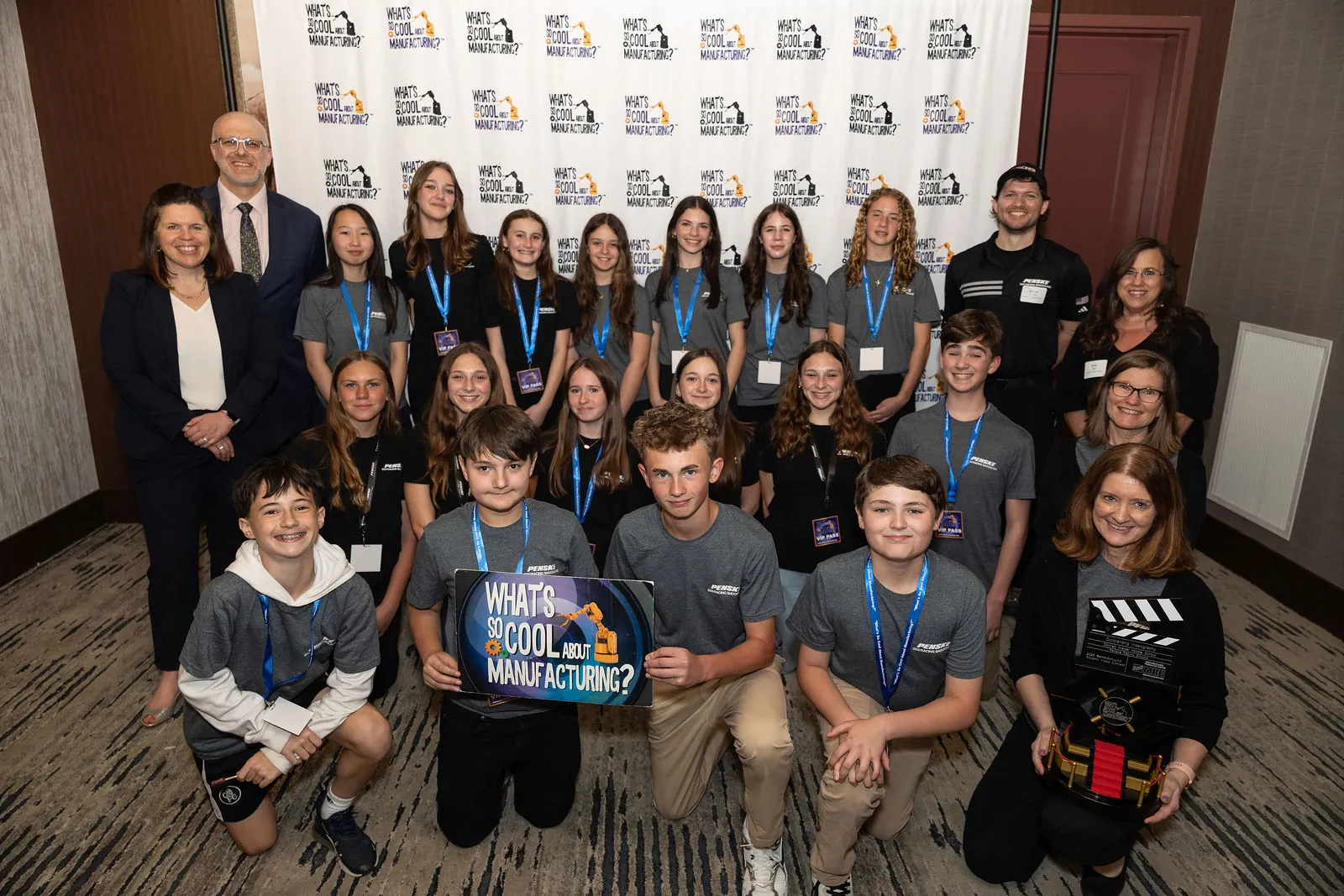 A large team in matching gray shirts posing with their trophy and contest signs at the step and repeat
