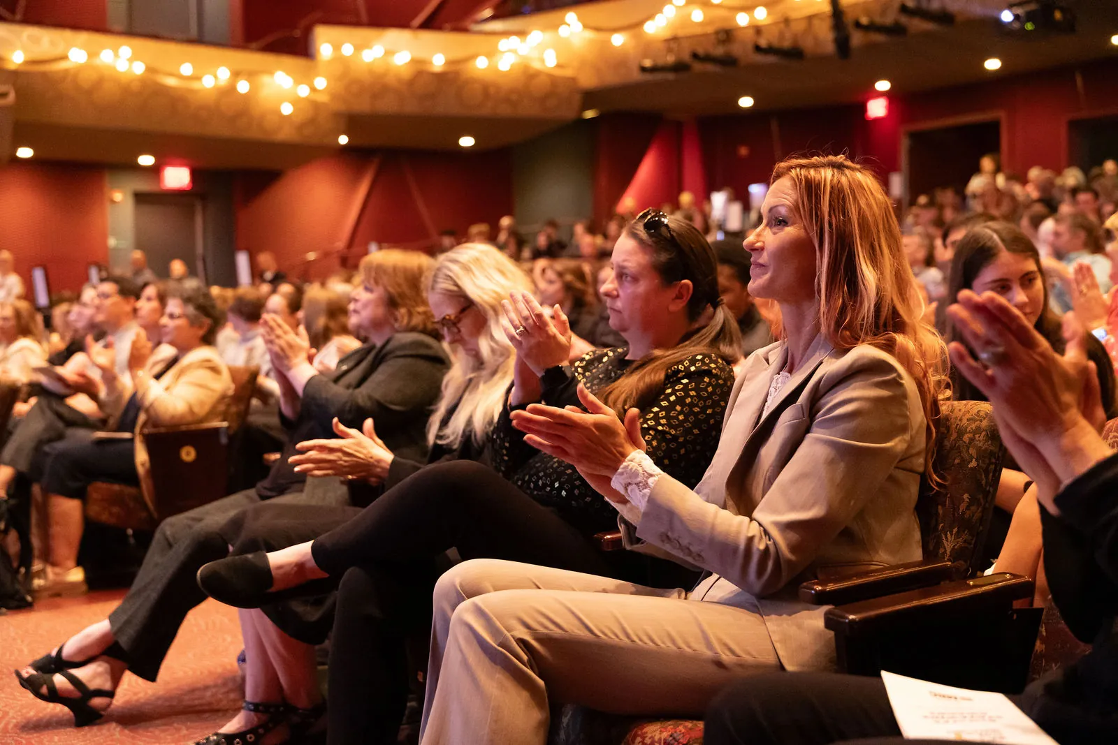 Adults in the front rows of the theater applauding