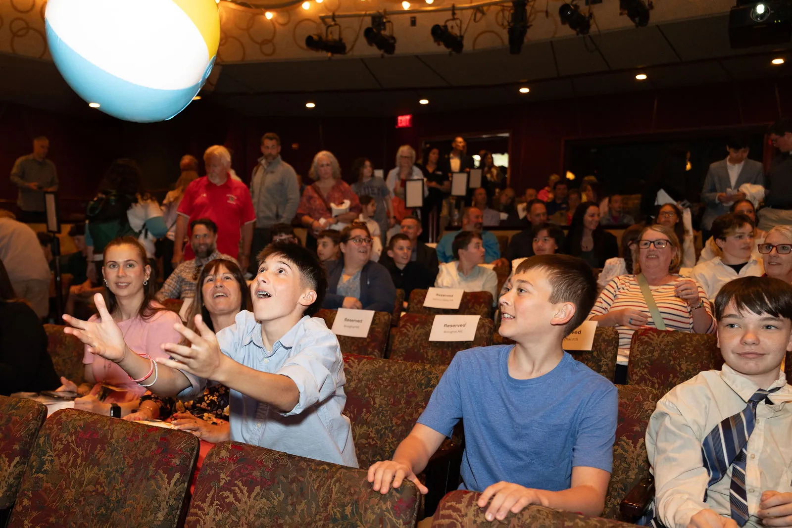A student reaching up to catch a beach ball in the theater seats