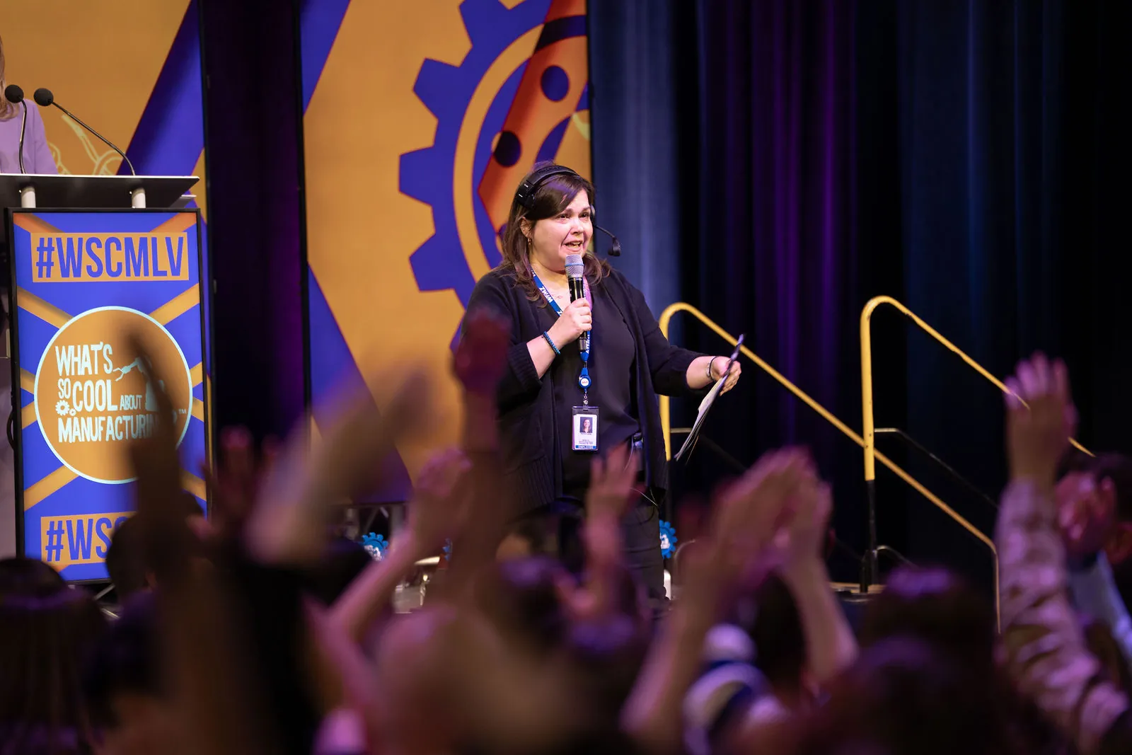 The crowd with hands in the air as a presenter with a headset mic works the stage