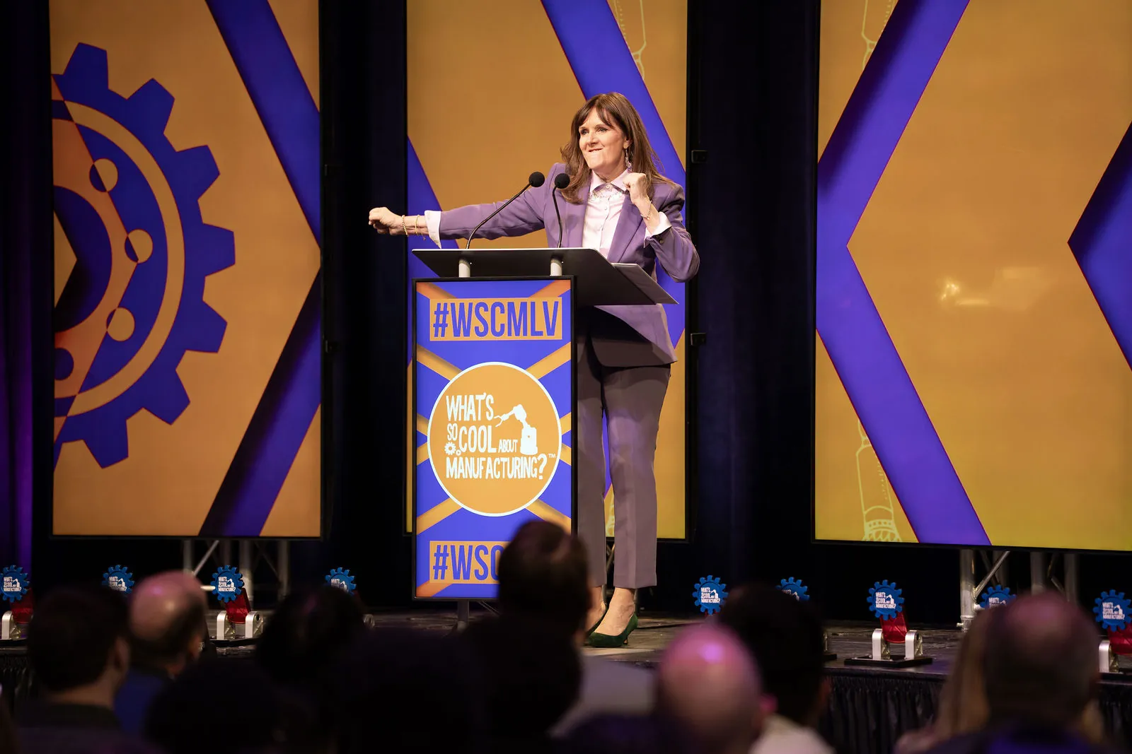 The host speaking at the #WSCMLV podium in front of the purple and gold stage set