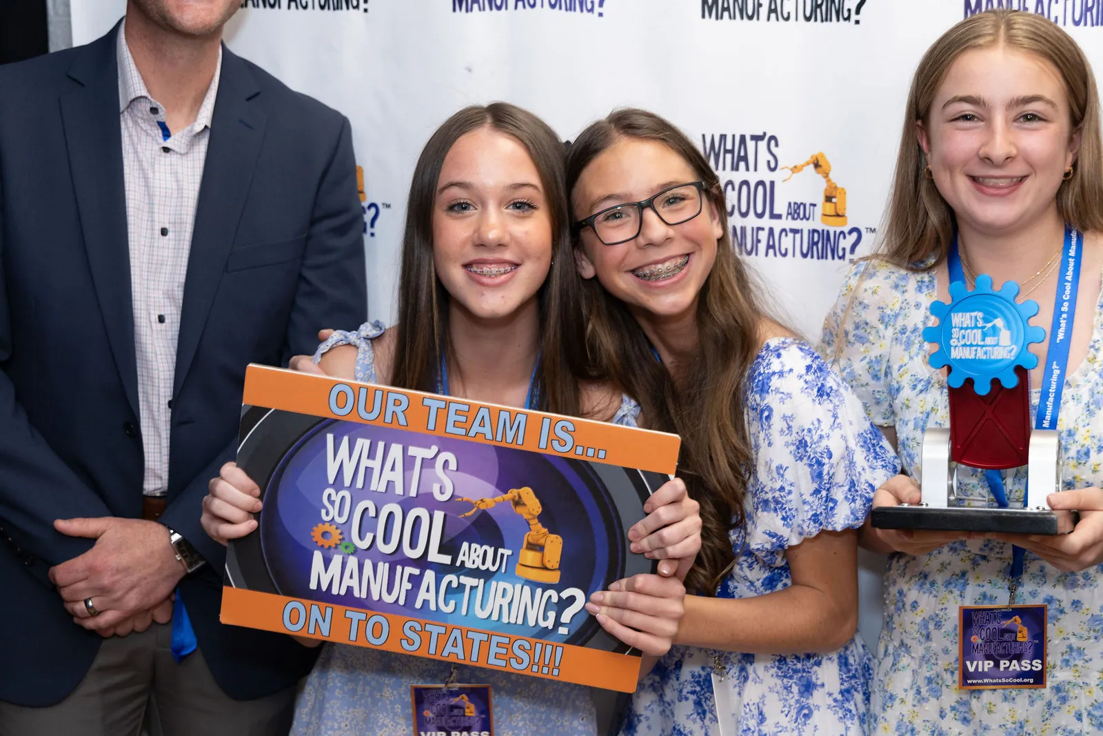 Three students holding an 'Our team is on to states' sign and their trophy at the step and repeat