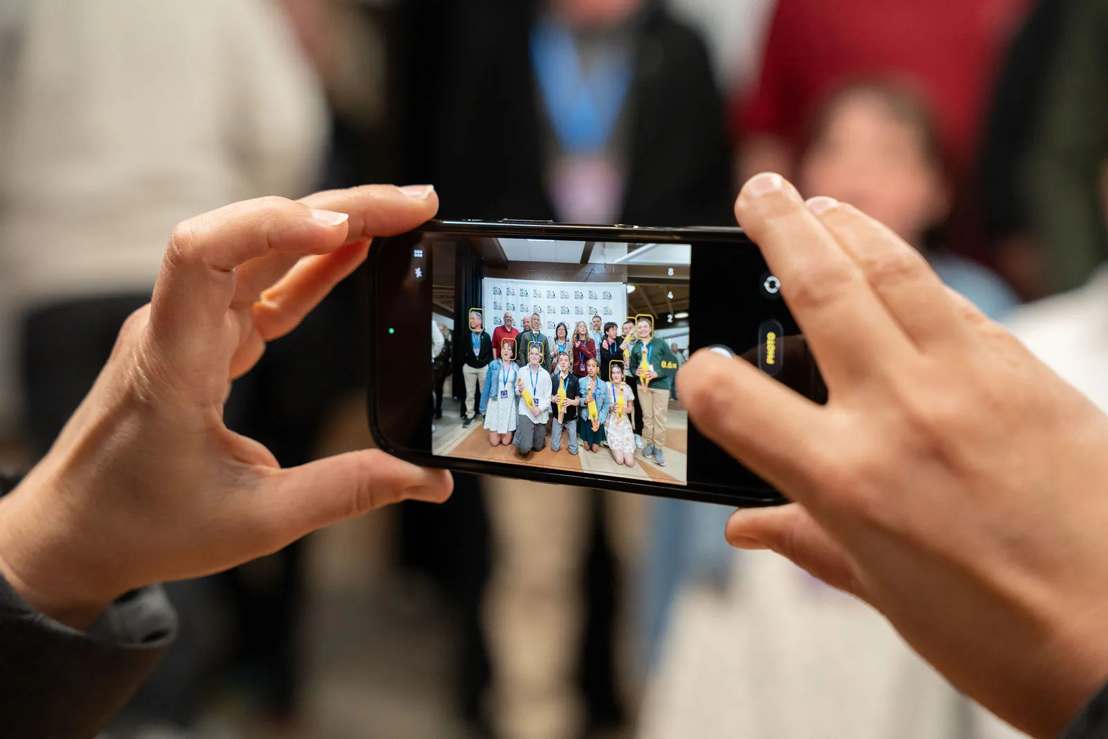 A parent taking a phone photo of a team at the step and repeat