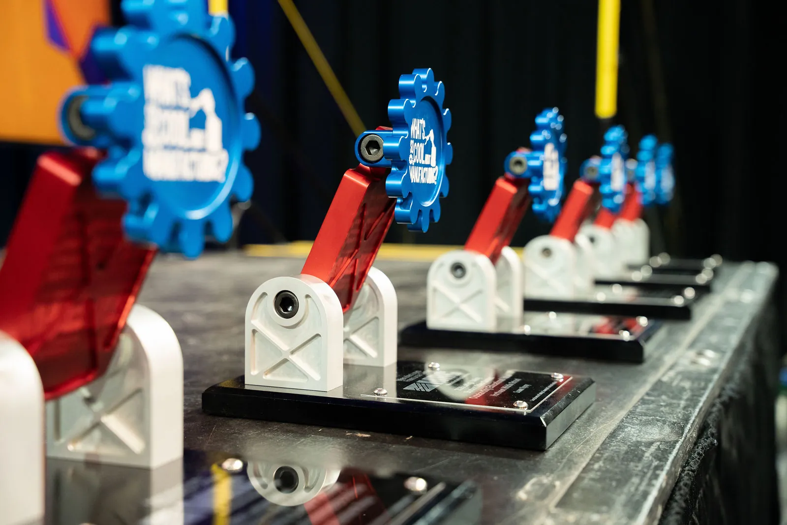 A row of What's So Cool About Manufacturing trophies, blue gears on red robot arms, lined up on the stage